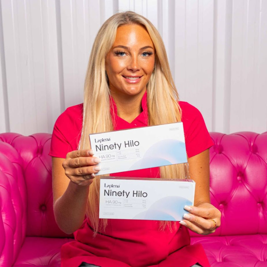 Woman sitting on a pink couch holding 'Ninety Hilo' products against a white curtain background.