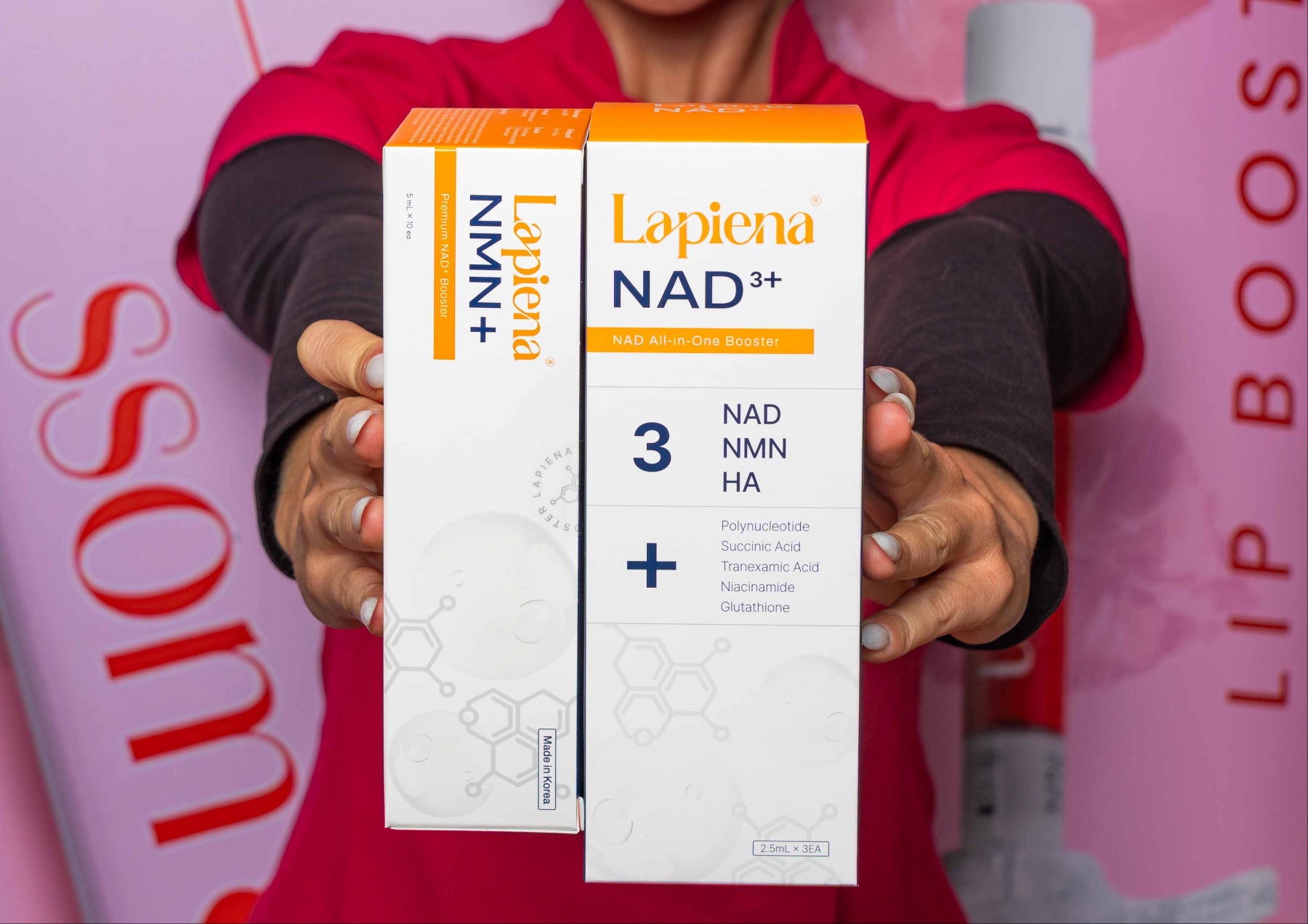 Woman holding a NAD3+ and NMN+ product boxes against a pink background 