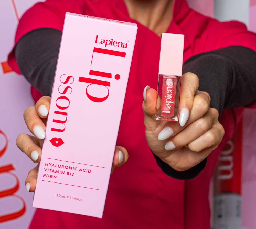 A person in a red top holds a pink Lapiena Lipssom lip booster and a matching pink lip gloss bottle